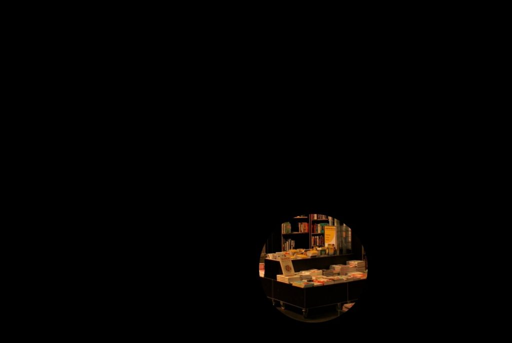The picture is black except from a small circle, which shows a close up on book shelves in a bookstore. This illustrates narrow attention while searching for a specific book.
